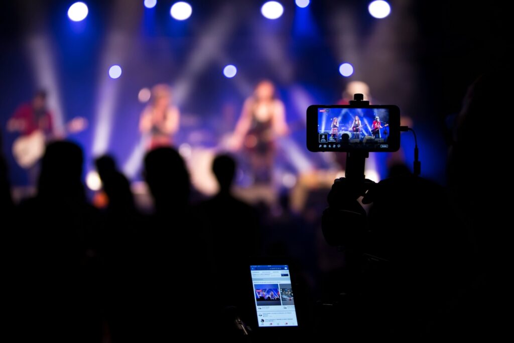 photo d'une foule de dos filmant un concert avec leur smartphone et étant sur des réseaux sociaux - l'importance des réseaux sociaux pour communiquer lors des événements musicaux - AVICOM' 
