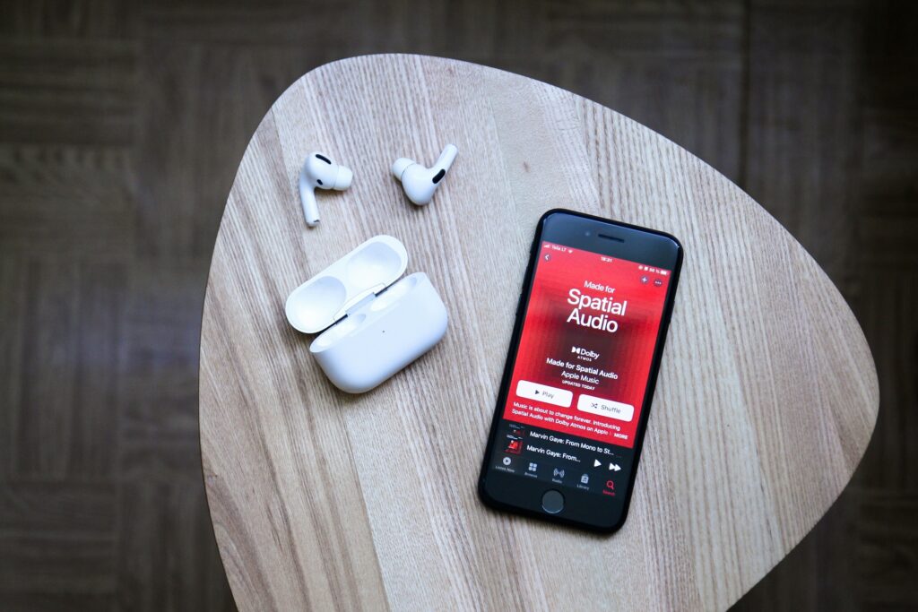 Photo d'un iPhone posé sur une table avec l'écran affichant Apple Music, AirPods posé à coté du téléphone - Communication et festivals - AVICOM'
