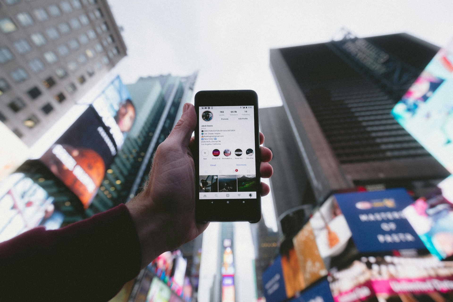 main d'un homme tenant un téléphone affichant une page Instagram de voyage au milieu de Times Square à New York
